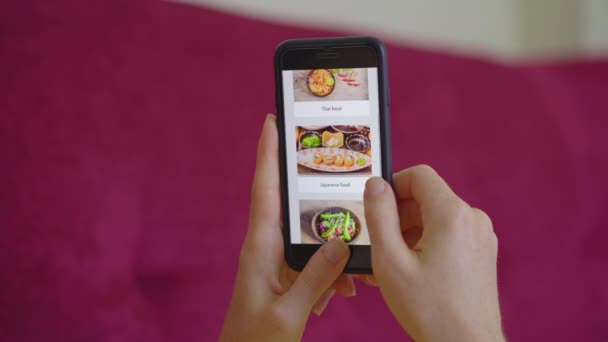 Fiatal nő megrendeli élelmiszer online segítségével egy okostelefon. Egy kanapén fekszik a lakásában. — Stock videók
