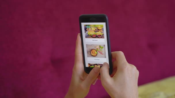 Mladá žena si objednává jídlo online pomocí chytrého telefonu. Leží na gauči ve svém bytě. — Stock video