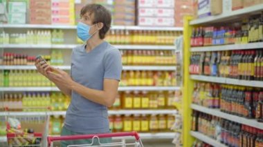 Telaşlı bir adam marketten ya da marketten yiyecek alırken Coronavirus 'a karşı tıbbi maske takar. Karantina bitti, artık giyim mağazasına gidebilirsin ama yüz maskesi takmak zorundasın. Sağlık