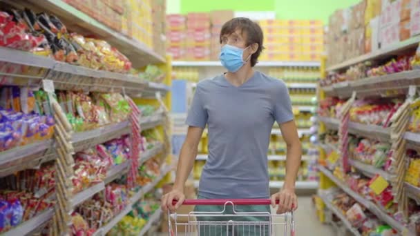 An alarmed man wears a medical mask against coronavirus while purchasing food in a supermarket or store. Quarantine is over, now you can go to the clothing store but have to wear a face mask. Health — Stock Video