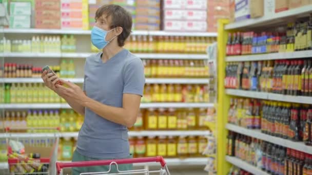 Un uomo allarmato indossa una maschera medica contro il coronavirus mentre acquista cibo in un supermercato o negozio. La quarantena è finita, ora puoi andare al negozio di abbigliamento ma devi indossare una maschera facciale. Sanità — Video Stock