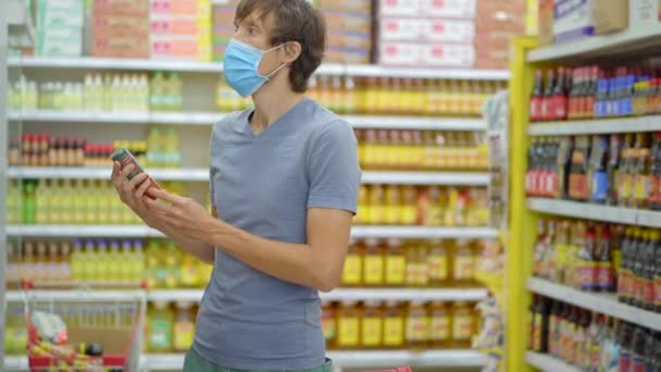 Um homem alarmado usa uma máscara médica contra o coronavírus enquanto compra comida em um supermercado ou loja. A quarentena acabou, agora você pode ir à loja de roupas, mas tem que usar uma máscara facial. Saúde — Vídeo de Stock