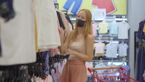 Een vrouw in een kledingwinkel met een medisch masker vanwege een coronovirus. Quarantaine is voorbij, nu kun je naar de kledingwinkel maar moet je een masker dragen. — Stockvideo