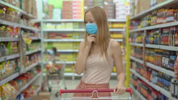 A riadt nőstény orvosi maszkot visel a koronavírus ellen, miközben élelmiszert vásárol egy szupermarketben vagy boltban. Vége a karanténnak, elmehetsz a ruhaboltba, de arcmaszkot kell viselned. Egészségügy — Stock videók