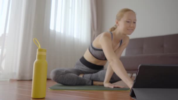 Fitness-Frau trainiert zu Hause auf dem Boden und schaut sich Fitness-Videos auf einem Tablet an. Menschen treiben wegen des Coronovirus online Sport. Fokus auf das Tablet — Stockvideo