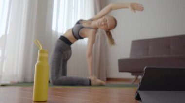 Spor salonundaki kadın evde egzersiz yapıyor ve tabletle spor salonu videoları izliyor. İnsanlar koronovirüs yüzünden spor yapıyor. Tablete odaklan.