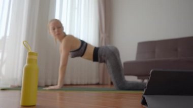 Spor salonundaki kadın evde egzersiz yapıyor ve tabletle spor salonu videoları izliyor. İnsanlar koronovirüs yüzünden spor yapıyor. Tablete odaklan.