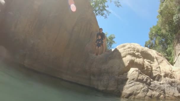 Zeitlupenaufnahme eines Vaters, der seinen Sohn von einer Klippe in einen Fluss wirft. Sommerzeit-Konzept — Stockvideo