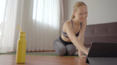 Spor salonundaki kadın evde egzersiz yapıyor ve tabletle spor salonu videoları izliyor. İnsanlar koronovirüs yüzünden spor yapıyor. Tablete odaklan.