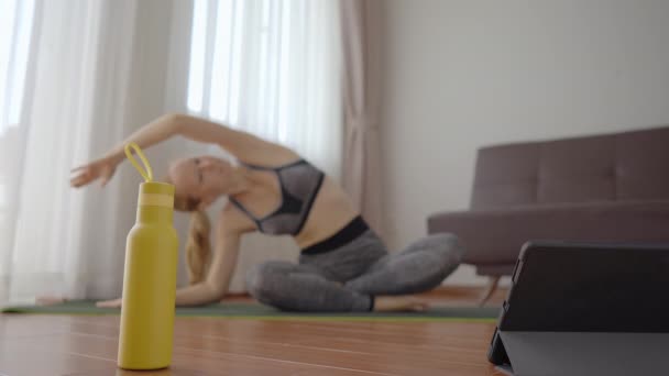 Fitnessvrouw die thuis op de vloer traint en fitnessvideo 's bekijkt in een tablet. Mensen sporten online vanwege het coronovirus. Focus op de tablet — Stockvideo