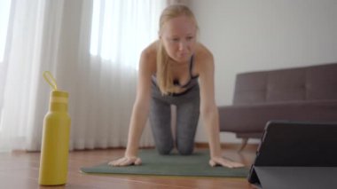 Spor salonundaki kadın evde egzersiz yapıyor ve tabletle spor salonu videoları izliyor. İnsanlar koronovirüs yüzünden spor yapıyor. Tablete odaklan.