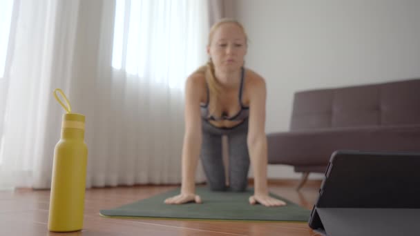 Fitnessvrouw die thuis op de vloer traint en fitnessvideo 's bekijkt in een tablet. Mensen sporten online vanwege het coronovirus. Focus op de tablet — Stockvideo