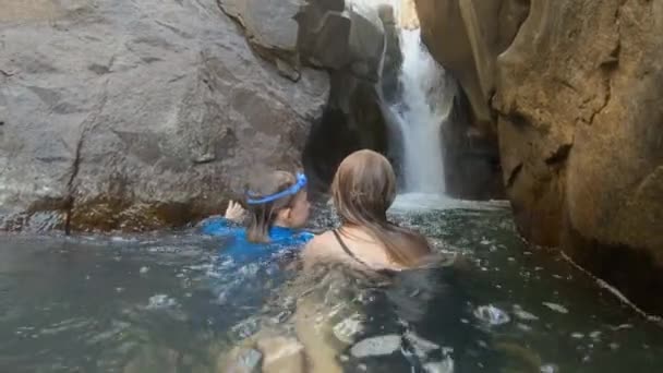 Scatto al rallentatore di una giovane donna e del suo figlioletto in un fiume tropicale con una cascata. Concetto di ora legale — Video Stock