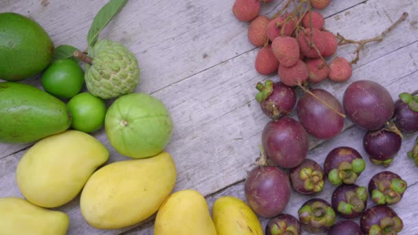 Жінка бере фрукти з дерев'яного столу, повного тропічних фруктів — стокове відео