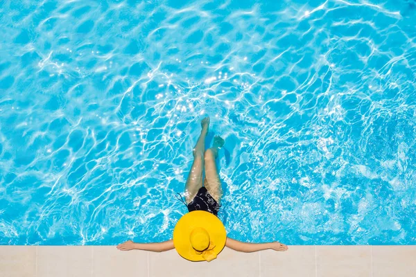 Frau sitzt in einem Schwimmbad in einem großen gelben Sonnenhut — Stockfoto