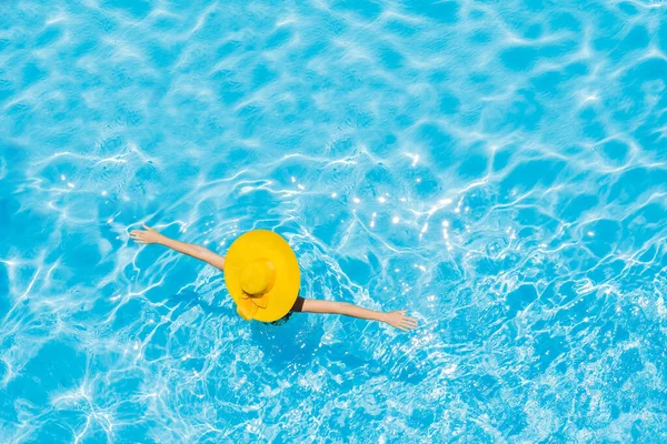 Mulher sentada em uma piscina em um grande chapéu de sol amarelo — Fotografia de Stock