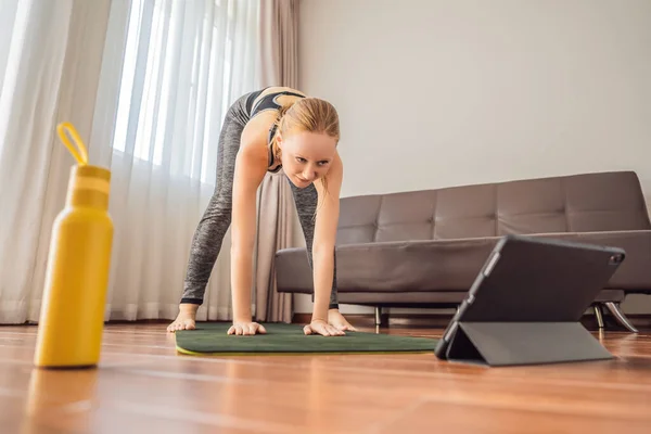 Donna fitness che si allena sul pavimento a casa e guarda i video di fitness in un tablet. La gente fa sport online a causa del coronovirus — Foto Stock