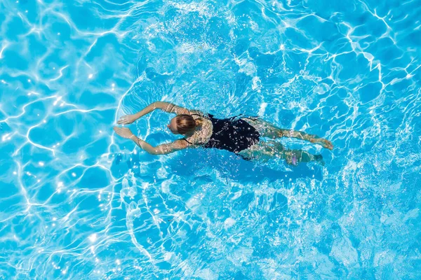 Mujer con traje de baño negro nadando en una piscina de agua azul —  Fotos de Stock