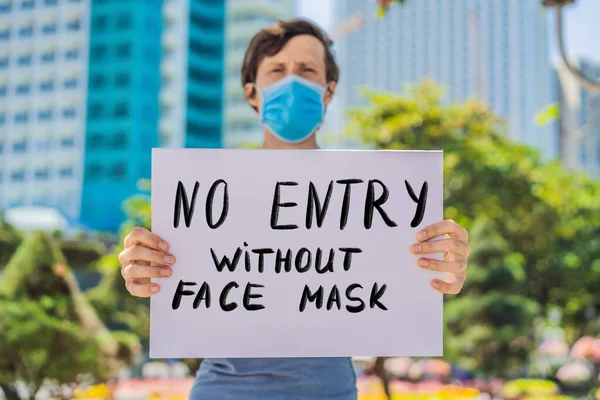 Tıbbi maskeli bir adam koronavirüs hastalığını önlüyor. Yüzünde maske olmayan bir poster taşıyor. El yazısı var. Coronovirus COVID 19 konsepti — Stok fotoğraf