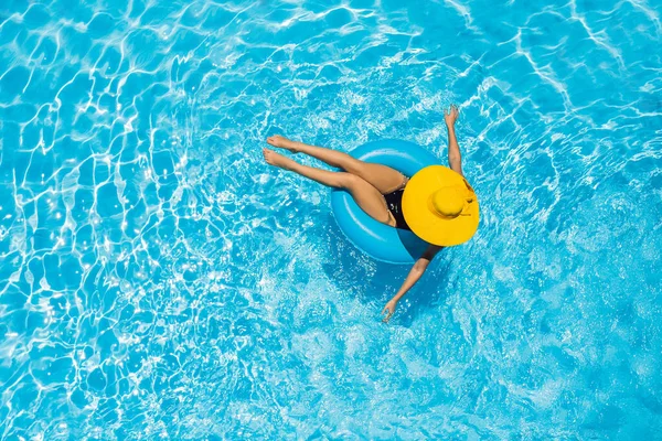 Frau, die in einem Schwimmbad auf einem Ringpool sitzt, schwimmt in einem großen gelben Sonnenhut — Stockfoto