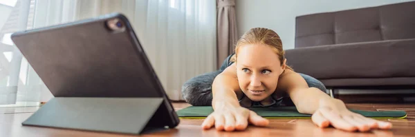 Mujer fitness haciendo ejercicio en el suelo en casa y viendo videos de fitness en una tableta. La gente hace deportes en línea debido al coronovirus BANNER, FORMATO LARGO — Foto de Stock