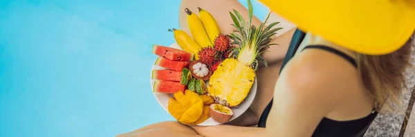 Молодая женщина отдыхает и ест фруктовую тарелку у бассейна отеля. Экзотическая летняя диета. Фото ног со здоровой пищей у бассейна, вид сверху. Тропический образ жизни на пляже Баннер, длинный Формат — стоковое фото