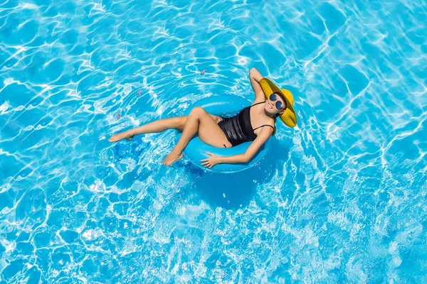 Woman sitting in a swimming pool on a ring pool float in a large yellow sunhat — Stock Photo, Image