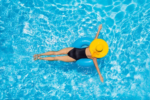 Mulher sentada em uma piscina em uma piscina anel flutuar em um grande chapéu de sol amarelo — Fotografia de Stock