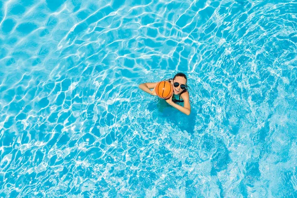 Jovem joga na piscina com uma bola de praia — Fotografia de Stock