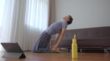 Evde yoga yapan genç bir adam tabletten izlediği bir videonun talimatlarını takip ediyor. Sosyal uzaklık kavramı. İnternet çalıştırıcı kavramı