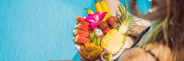 Jovem relaxante e comendo prato de frutas na piscina do hotel. Dieta de verão exótica. Foto de pernas com comida saudável à beira da piscina, vista superior de cima. Estilo de vida na praia tropical BANNER, LONG FORMAT — Fotografia de Stock