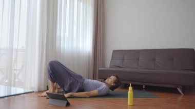 Evde yoga yapan genç bir adam tabletten izlediği bir videonun talimatlarını takip ediyor. Sosyal uzaklık kavramı. İnternet çalıştırıcı kavramı
