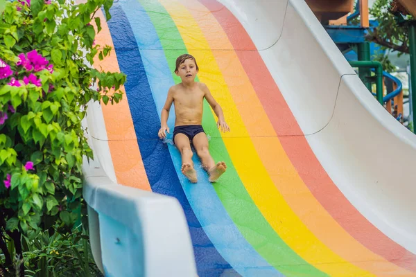 Мальчику или ребенку весело плескаться в бассейн после спуска по водной горке летом — стоковое фото