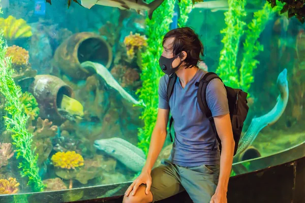 De mens met medische maskers kijkt naar de vissen in het aquarium in het oceanarium. Mensen lopen in medische maskers na het einde van het coronovirus — Stockfoto