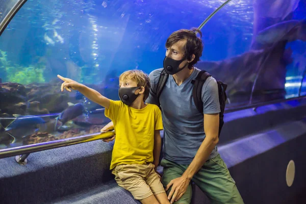 Papà e figlio in maschere mediche guardano i pesci nell'acquario in oceanario. La gente cammina in maschere mediche dopo la fine del coronovirus — Foto Stock