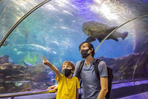 Pa en zoon met medische maskers kijken naar de vissen in het aquarium in het oceanarium. Mensen lopen in medische maskers na het einde van het coronovirus — Stockfoto