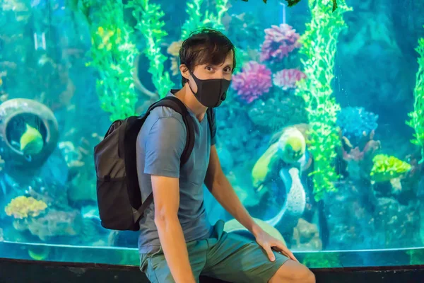 Man in medical masks look at the fish in the aquarium in oceanarium. People walk in medical masks after the end of the coronovirus — Stock Photo, Image