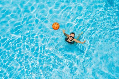 Genç bir kadın plaj topuyla havuzda oynuyor.
