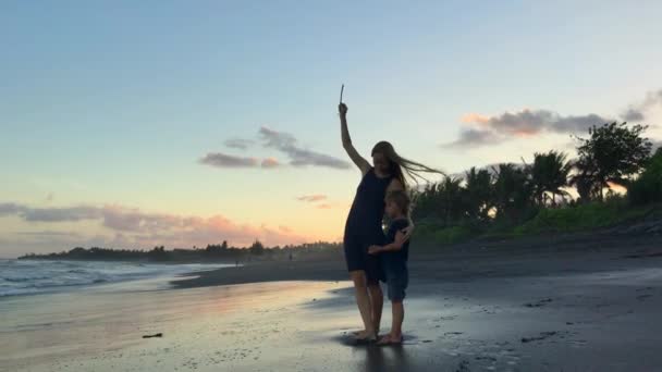 Uma jovem mulher e o seu filho com um papagaio numa praia. Tiro em um telefone — Vídeo de Stock