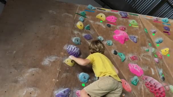 Ein kleiner Junge klettert in einer Boulderhalle die Wand hinauf. Schuss auf ein Handy — Stockvideo