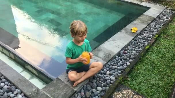 Маленький мальчик пьет фруктовый коктейль из стакана, используя соломинку из нержавеющей стали. Сократить использование пластика. Застрелен по телефону — стоковое видео