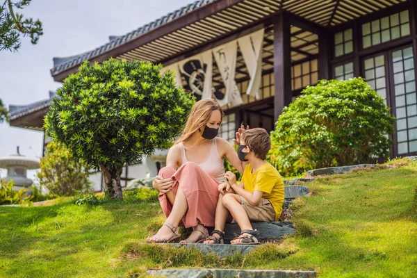 Matka a syn cestovatelé v lékařské masce se zastavili na ulici a pohlédli na tradiční japonskou budovu. Turisté cestují po epidemii koronaviru do Japonska — Stock fotografie