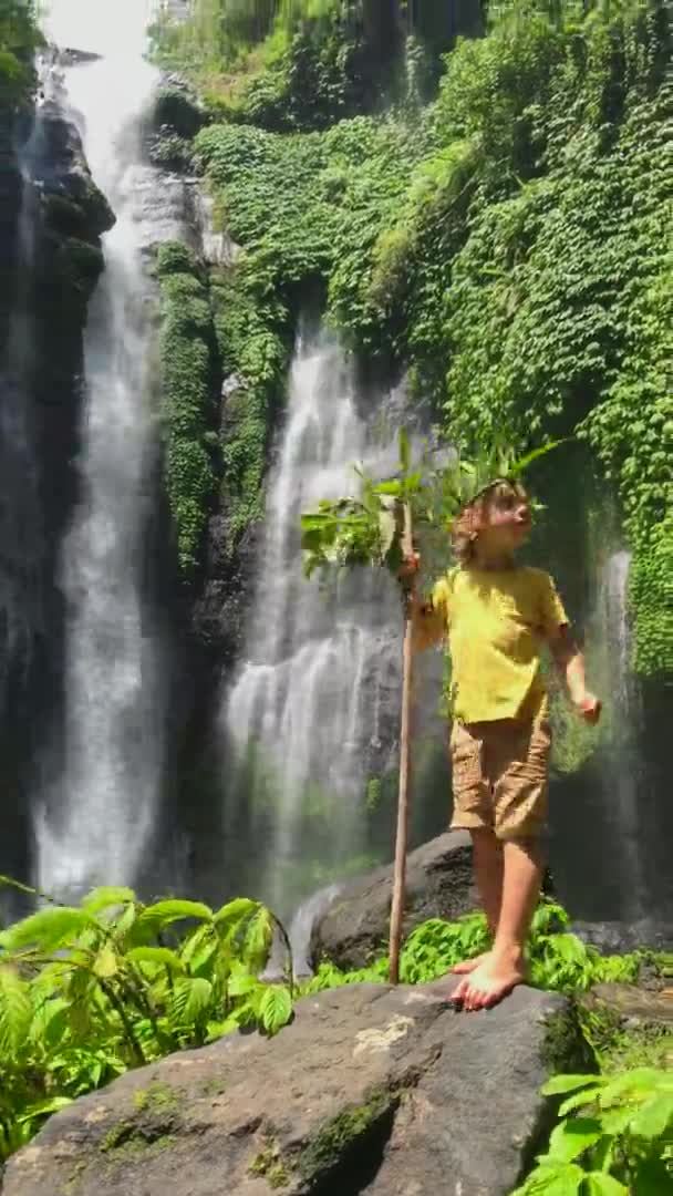 Video verticale. Un bambino divertente visita la cascata Sekumpul, la più grande cascata dell'isola di Bali. Girato su un telefono — Video Stock