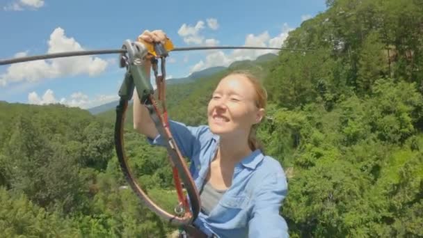 A young woman rides a zip line in an adventure park. She wears a safety harness. Outdoor amusement center with climbing activities consisting of zip lines and all sorts of obstacles. Slowmotion video — Stock Video