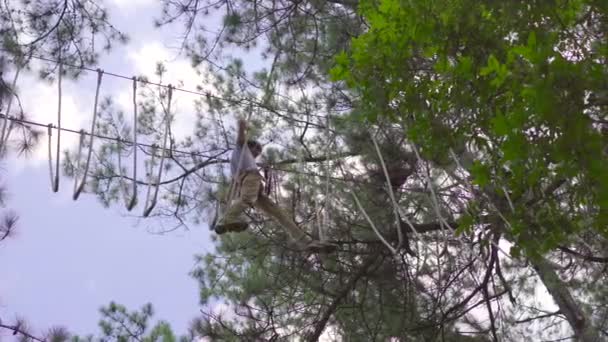 Un jeune homme dans un parc d'aventure. Il porte un harnais de sécurité. Il grimpe sur un sentier de corde haute. Centre de divertissement extérieur avec des activités d'escalade comprenant des tyroliennes et toutes sortes d'obstacles