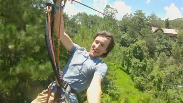 冒険公園でジップラインに乗る青年。彼は安全ハーネスをつけている。彼は高いロープの道を登る。ジップラインやあらゆる種類のクライミングアクティビティを備えた屋外アミューズメントセンター — ストック動画