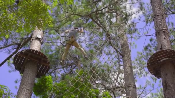 Un jeune homme dans un parc d'aventure. Il porte un harnais de sécurité. Il grimpe sur un sentier de corde haute. Centre de divertissement extérieur avec des activités d'escalade comprenant des tyroliennes et toutes sortes d'obstacles