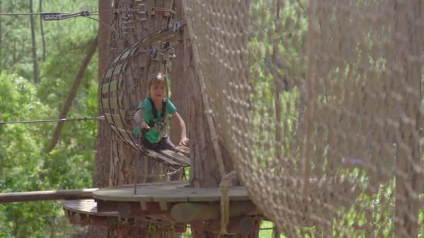 Un petit garçon dans un parc d'aventure. Il porte un harnais de sécurité. Il grimpe sur un sentier de corde haute. Centre de divertissement extérieur avec des activités d'escalade comprenant des tyroliennes et toutes sortes d'obstacles