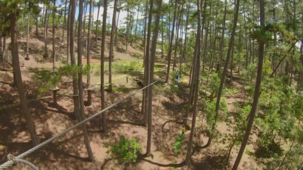A young woman rides a zip line in an adventure park. She wears a safety harness. Outdoor amusement center with climbing activities consisting of zip lines and all sorts of obstacles. Slowmotion video — Stock Video