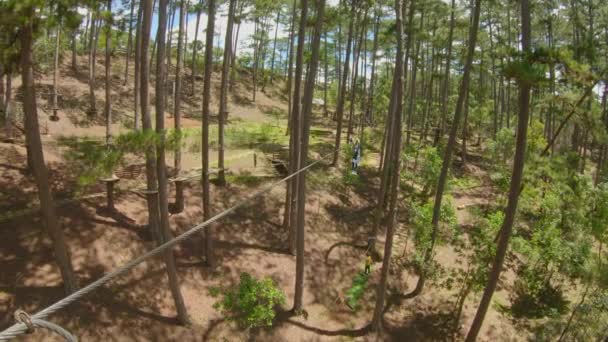 Uma jovem monta uma tirolesa em um parque de aventuras. Ela usa um cinto de segurança. Centro de diversões ao ar livre com atividades de escalada consistindo de tirolesa e todos os tipos de obstáculos. Vídeo em câmara lenta — Vídeo de Stock